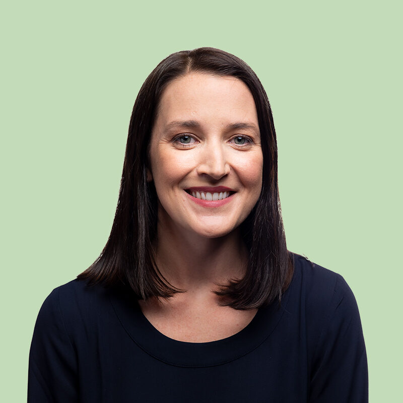 A woman with straight dark hair and a black top smiles at the camera against a light green background.