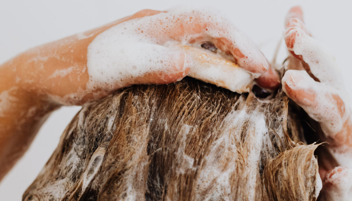 Close-up of a person washing their hair, with hands lathered in soap and shampoo suds.