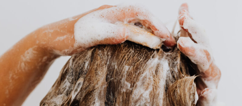 Close-up of a person washing their hair, with hands lathered in soap and shampoo suds.