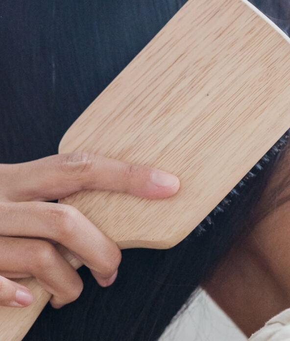 Person brushing long, dark hair with a wooden paddle brush.