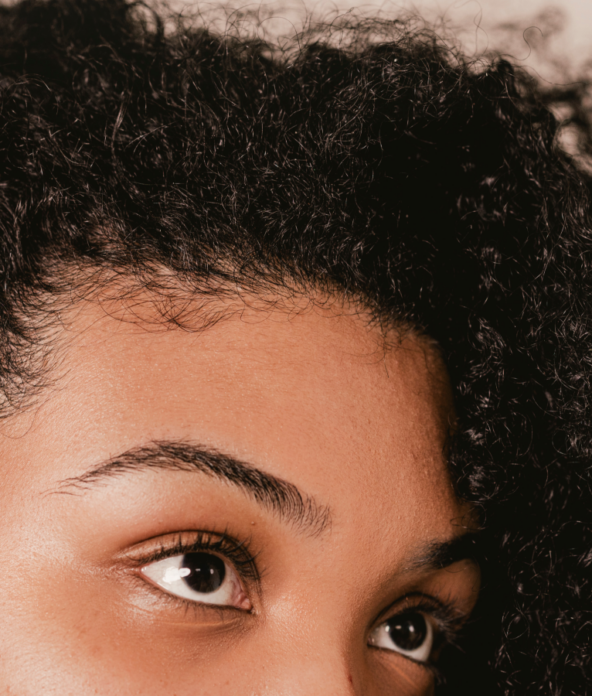 Close-up of a person with curly black hair and brown eyes, gazing upwards.