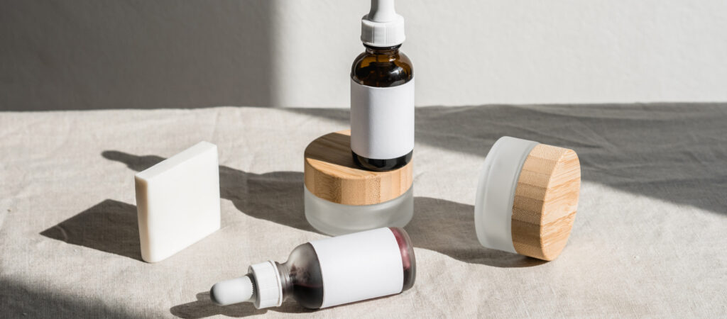 Skincare products with white labels and wooden lids on a beige cloth, featuring bottles with dropper caps and a rectangular soap bar.