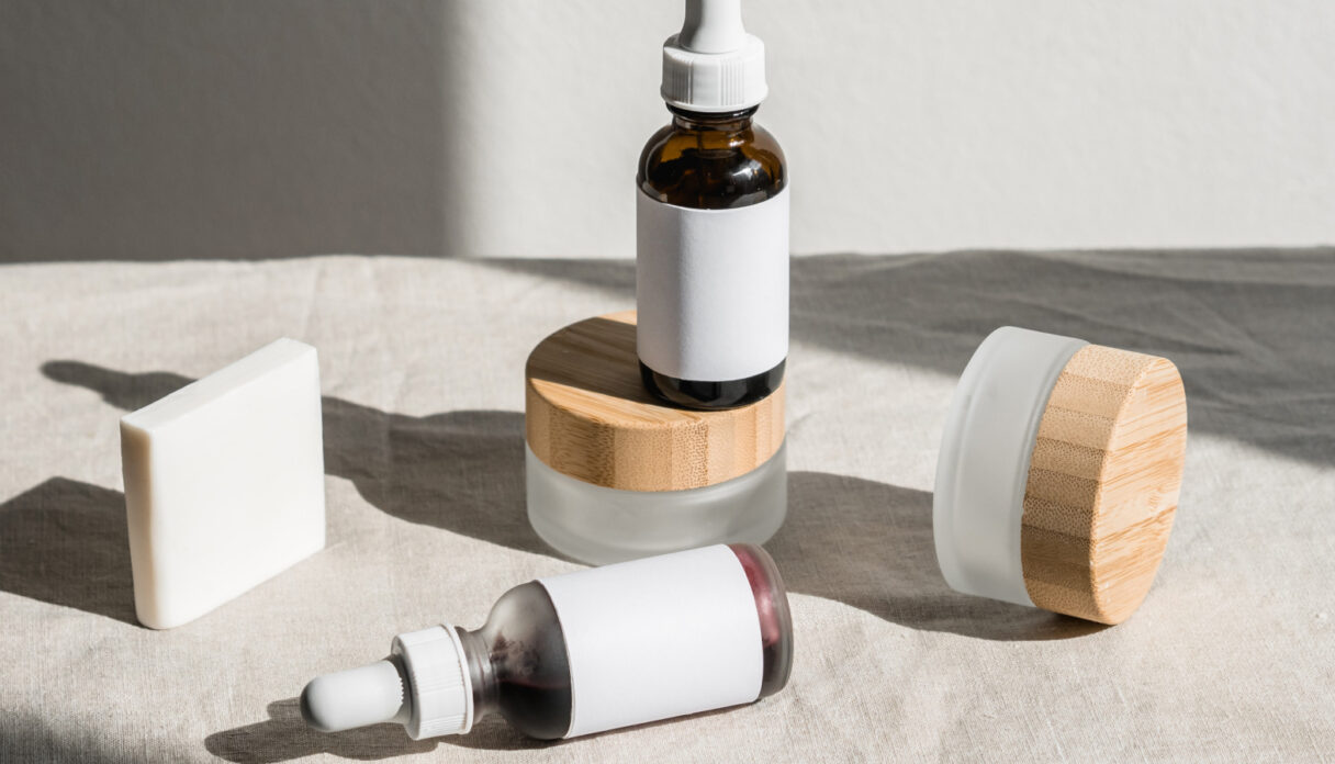 Skincare products with white labels and wooden lids on a beige cloth, featuring bottles with dropper caps and a rectangular soap bar.